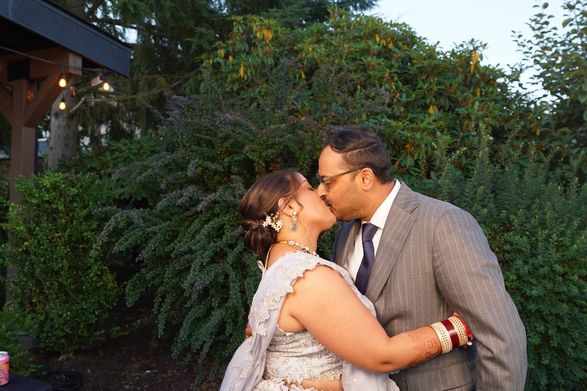 The couple kissing in a booth photo, greenery behind them