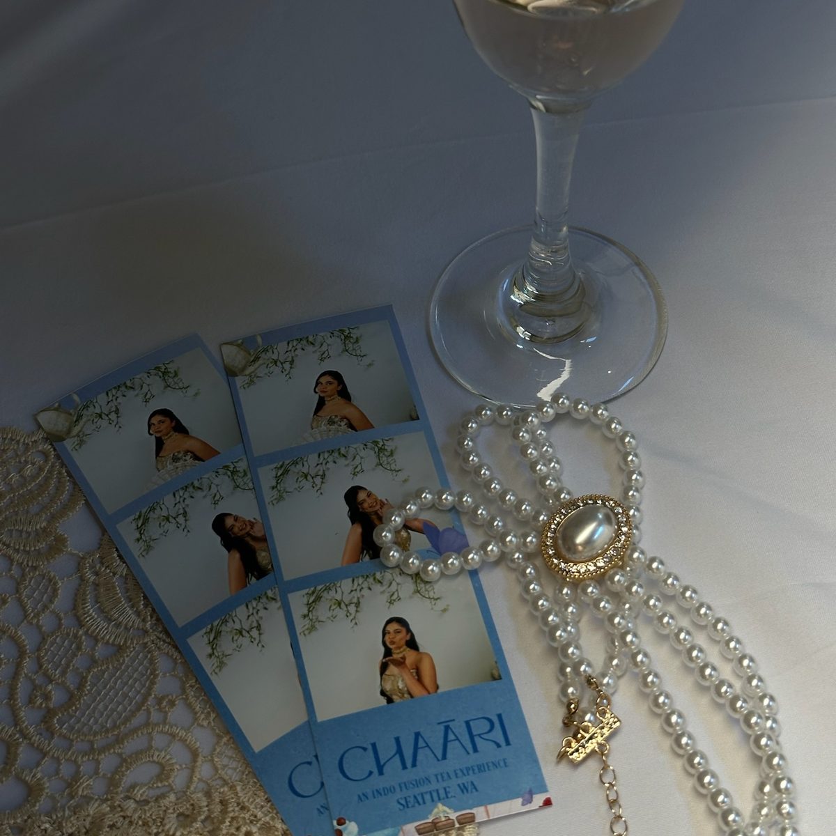 Printed strips from the brand event on lace beside pearls and a glass of champagne
