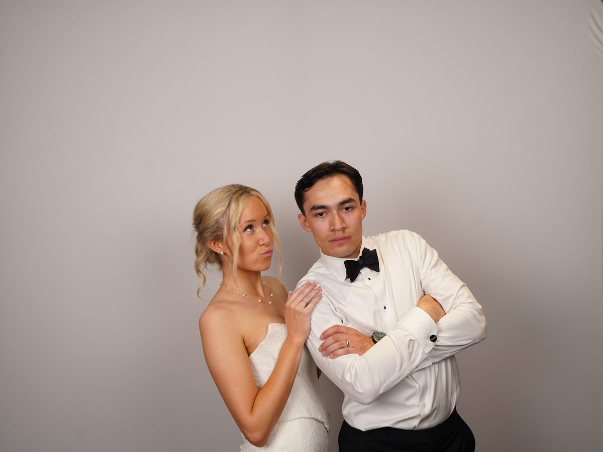 The couple in front of the white backdrop, the groom in a white dinner jacket