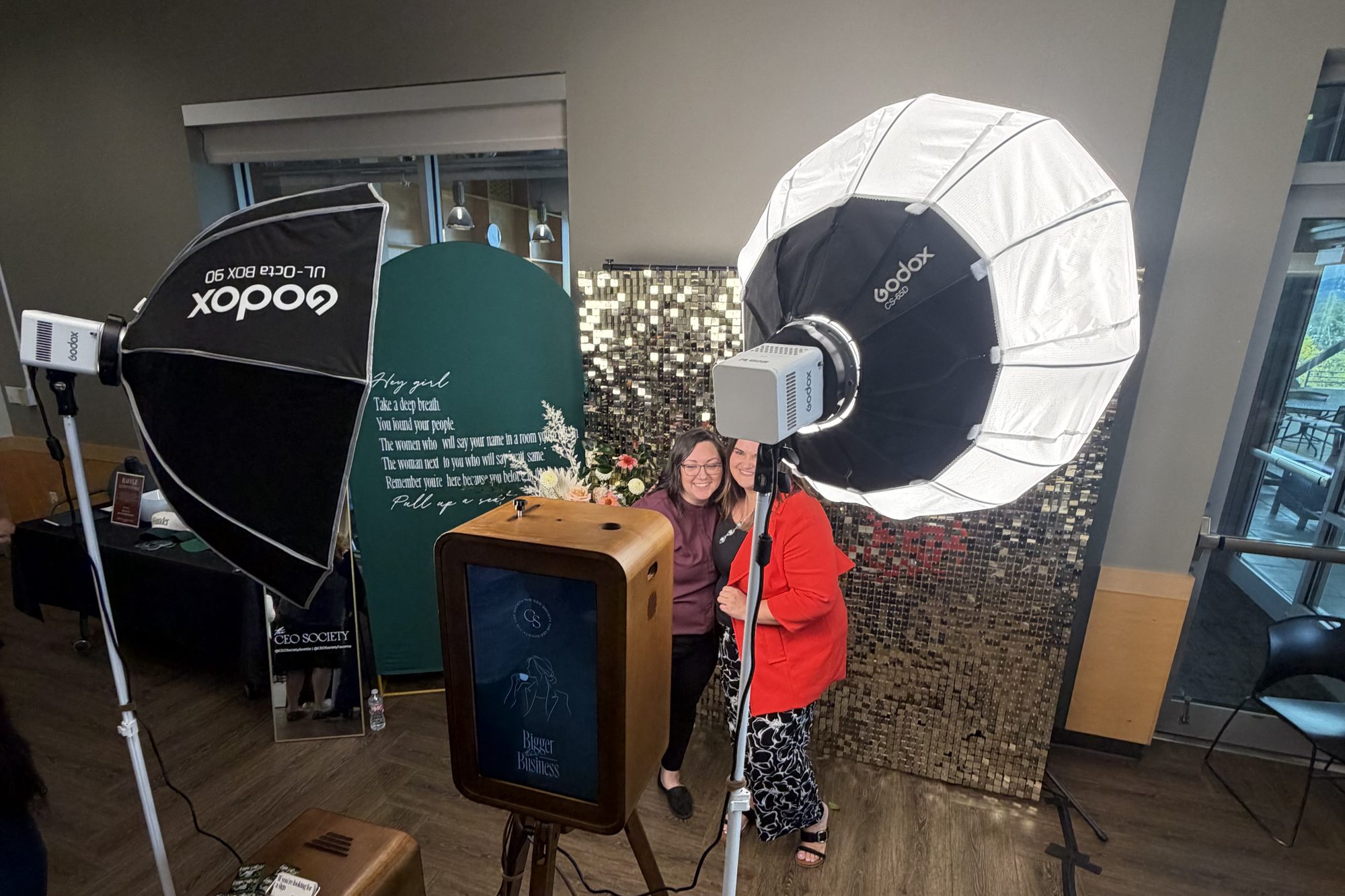 The open-air wood photo booth in a reception room, two guests posing between the softbox lights in front of a sequin wall