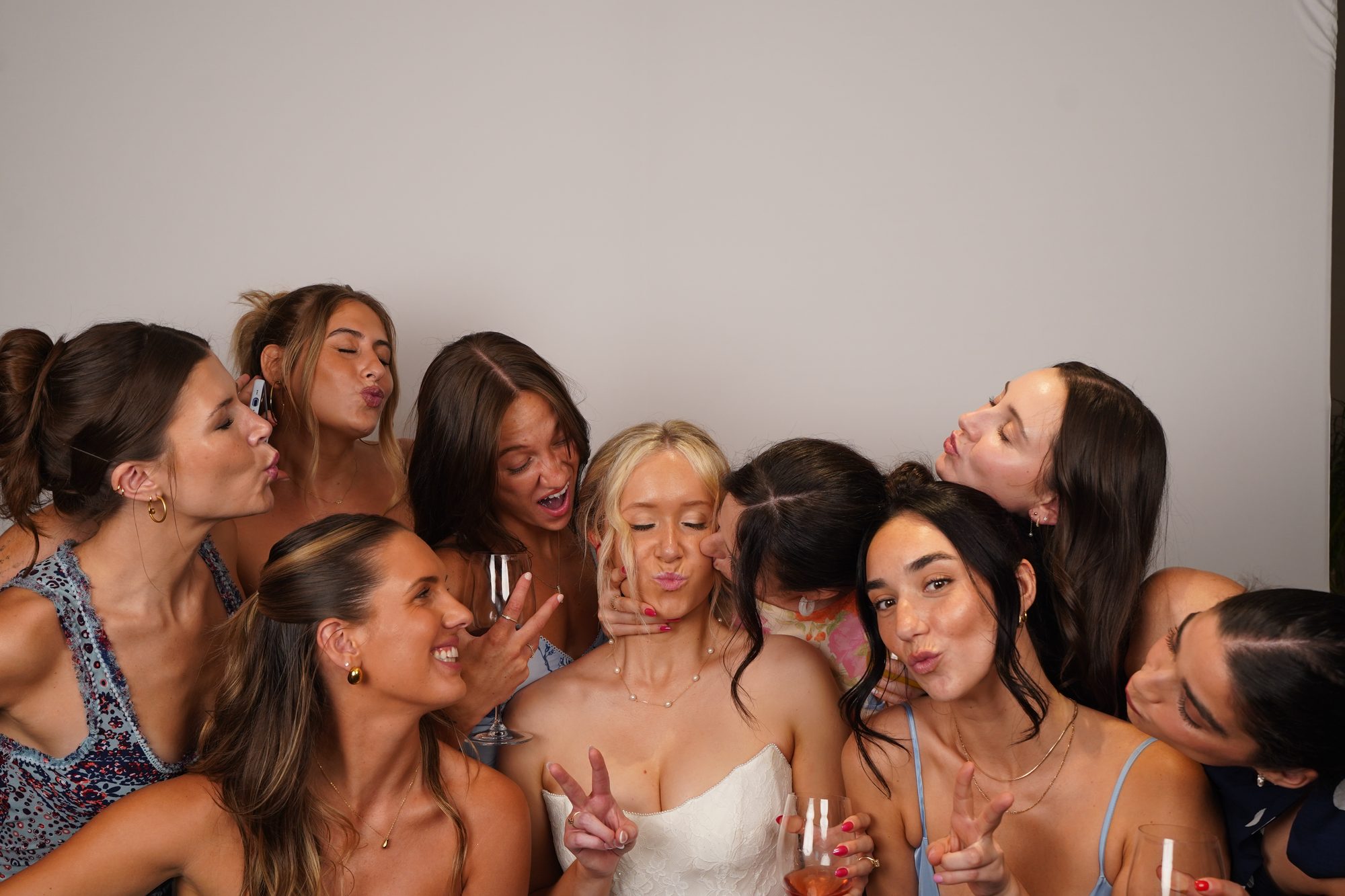 A booth photo from a wedding: the bride and her friends crowded together on the white backdrop, mid-laugh