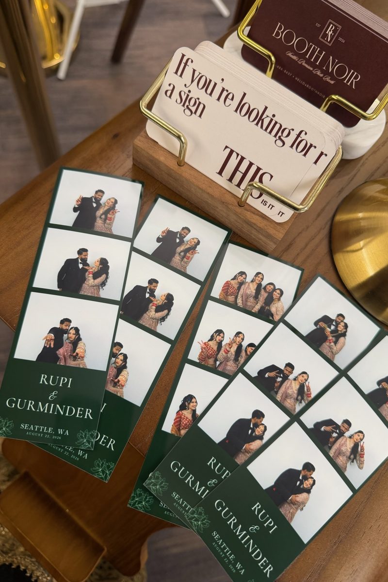 A spread of printed photo strips from Rupi and Gurminder's reception on the booth's side table, beside a Booth Noir card that reads 'If you're looking for a sign'
